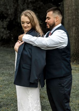 A sweet embrace between newlyweds outdoors, with the bride in white and groom in formal navy attire.