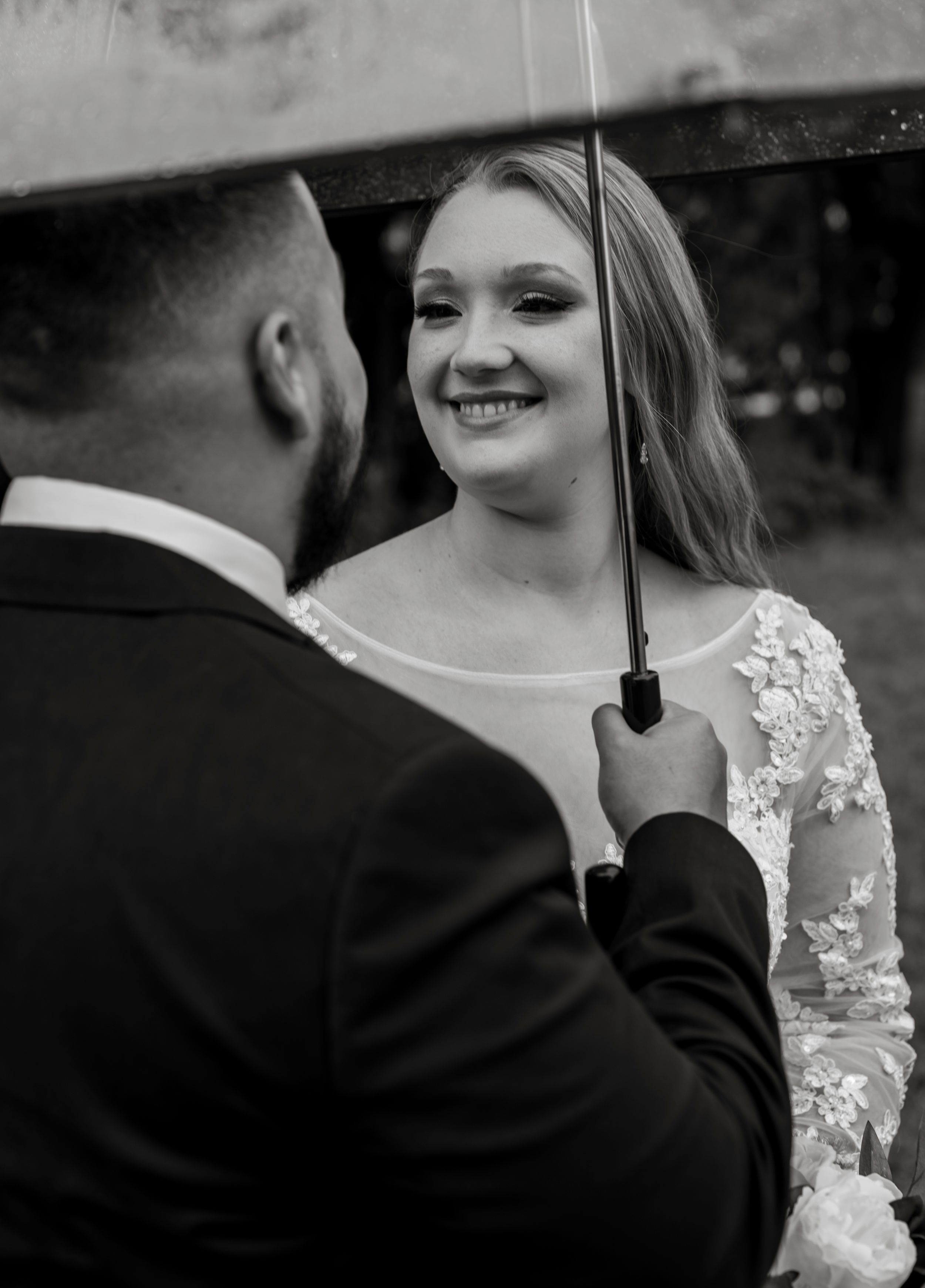 A tender moment captured under a clear umbrella during a rainy wedding day.