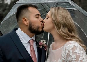 A romantic kiss shared under a clear umbrella during an outdoor wedding photo session.