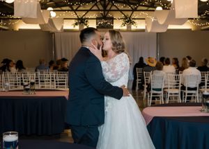 A couple shares their first dance in an elegant reception hall decorated with string lights and white chairs.