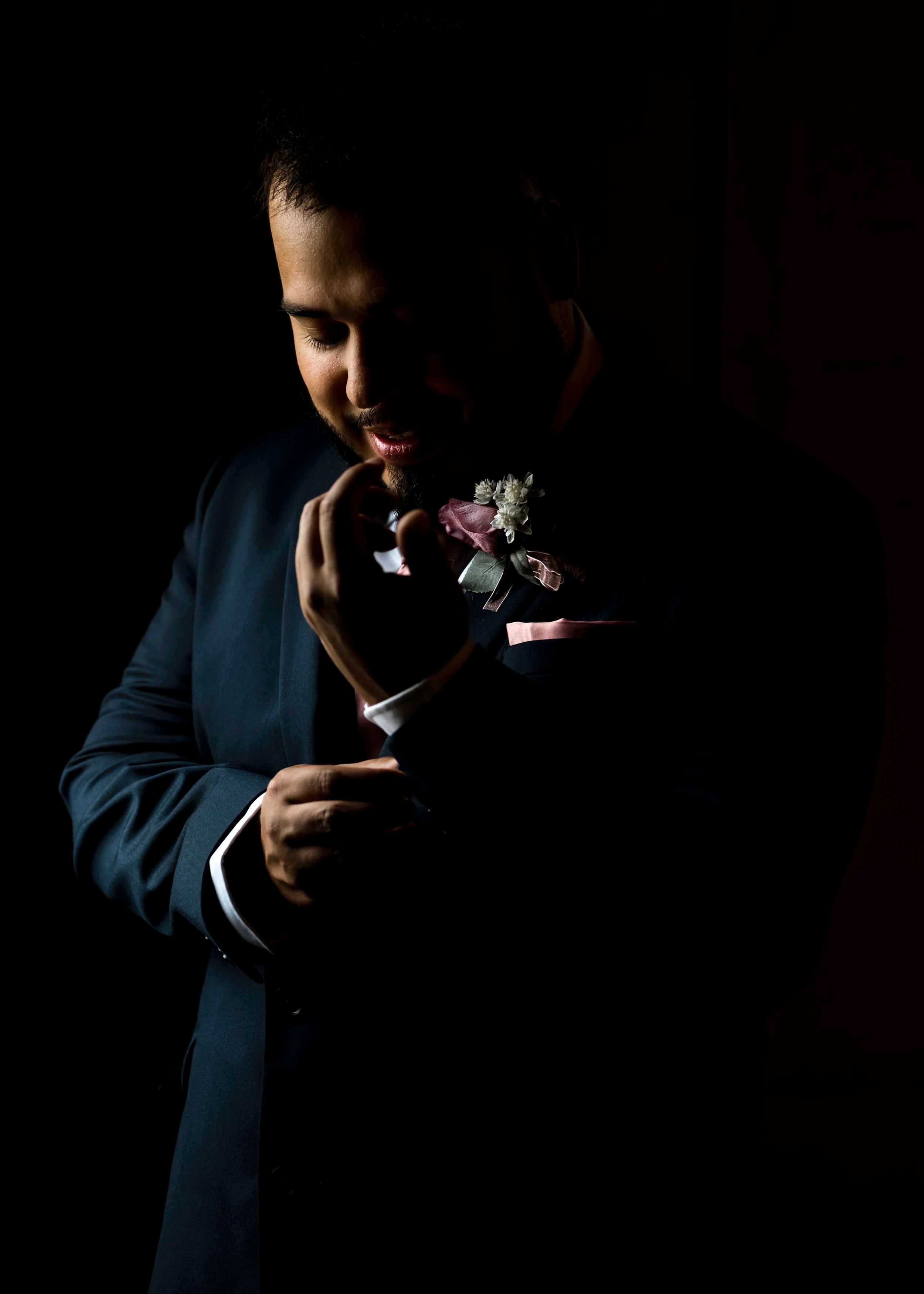 Artistic low-key portrait of someone in a navy suit holding a delicate flower in dramatic lighting.