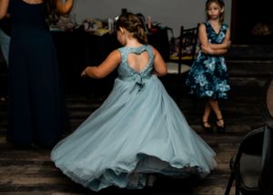 Young dancer twirls in a flowing light blue dress on a wooden dance floor.