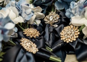 Wedding bouquets with blue flowers and ornate golden brooch details against dark fabric.