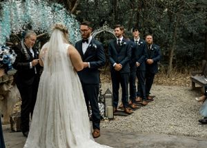 Wedding ceremony with groomsmen lined up under floral arch.