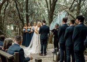 Outdoor forest wedding ceremony with bridesmaids in navy dresses.