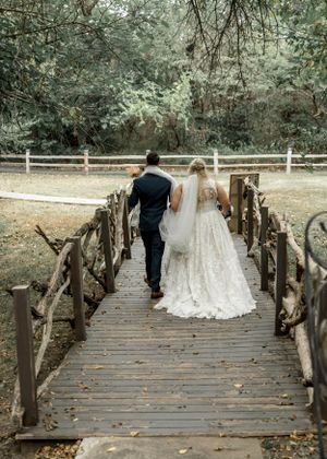 Newlyweds walk across rustic wooden bridge surrounded by forest.