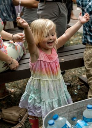 Young child in rainbow dress celebrating joyfully at outdoor event.