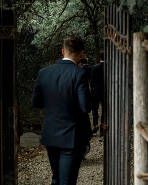 A suited figure walks through an ornate garden gate at dusk.