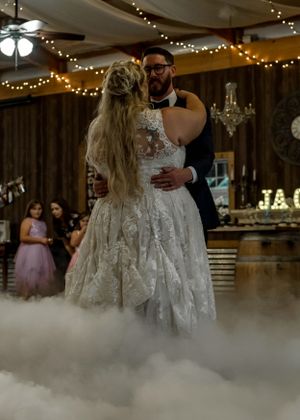 Newlyweds share their first dance surrounded by romantic fog and twinkling lights.
