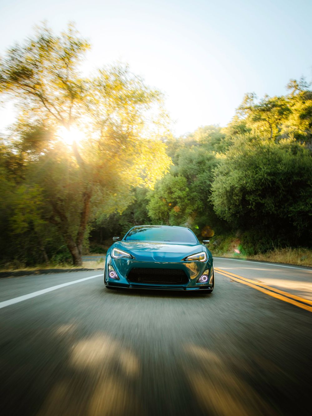 A teal Toyota GT86 at sunset driving through a winding mountain road.