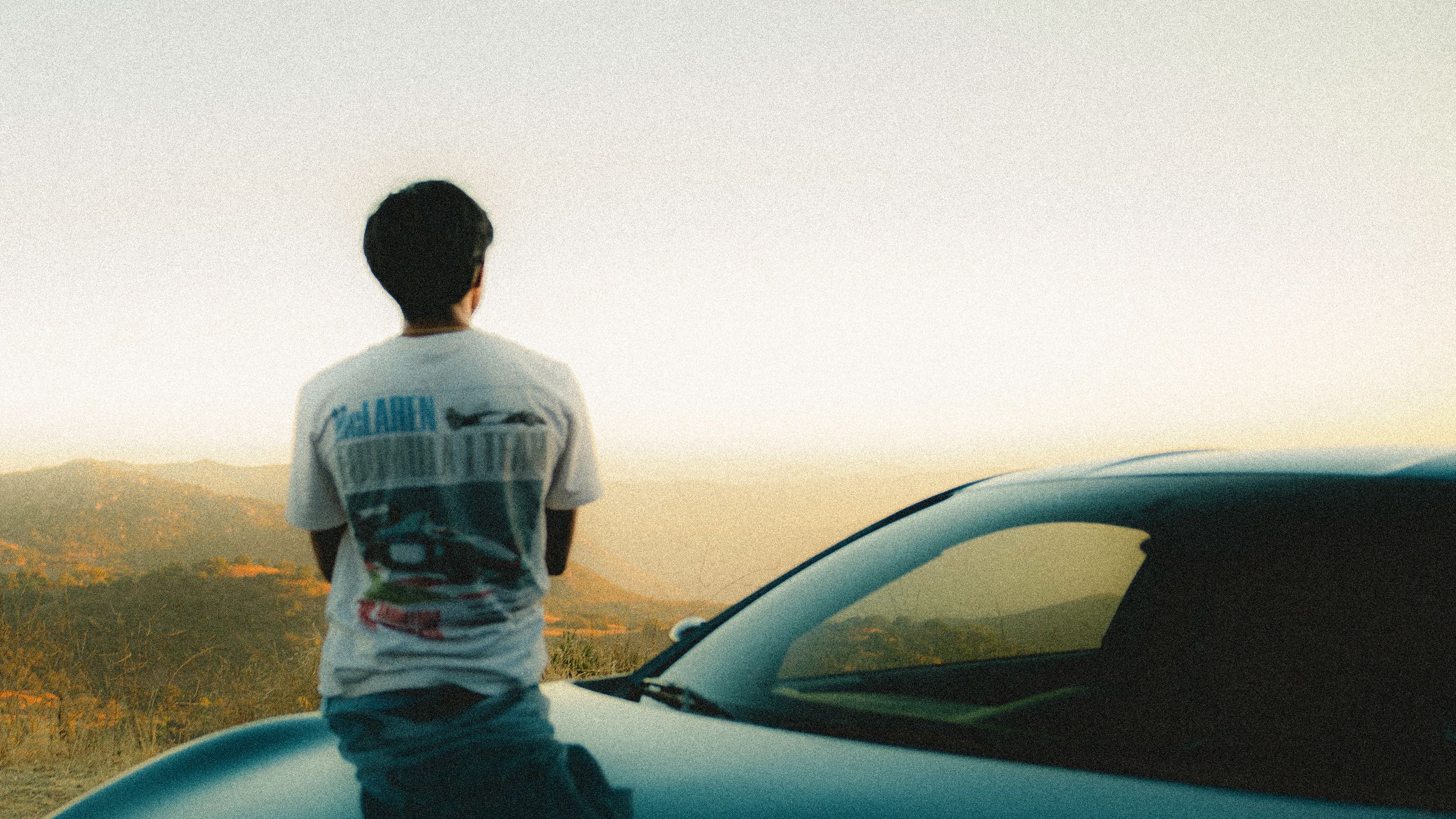 Person drives their Toyota GT86 at sunset along a winding mountain road overlooking scenic valleys and hills.