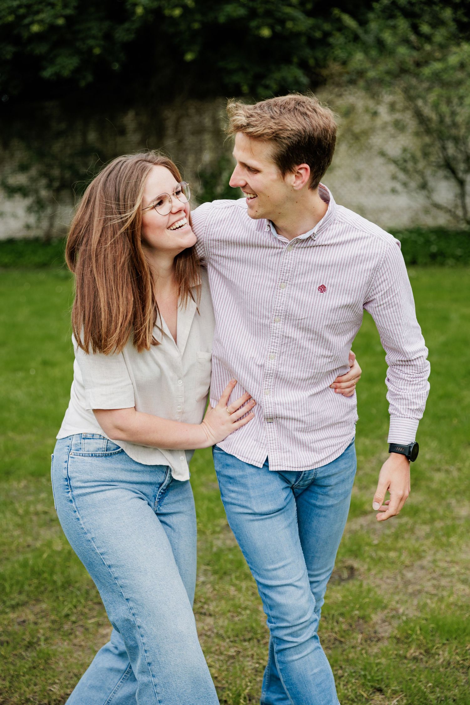 A playful couple in jeans laughing and embracing outdoors on a sunny day.