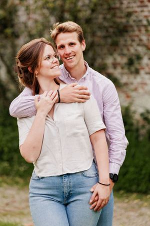 A romantic couple in casual attire sharing tender moments against a brick wall.