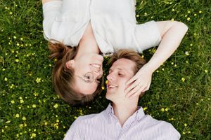 A couple lying in grass filled with yellow flowers sharing a romantic moment.