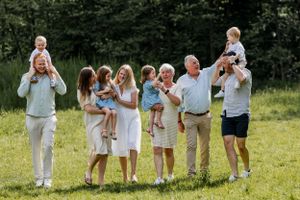 Group portrait of family members sitting together in a grassy meadow on a bright summer day.