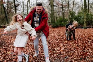 Family plays together in a park filled with fallen autumn leaves on a crisp day.