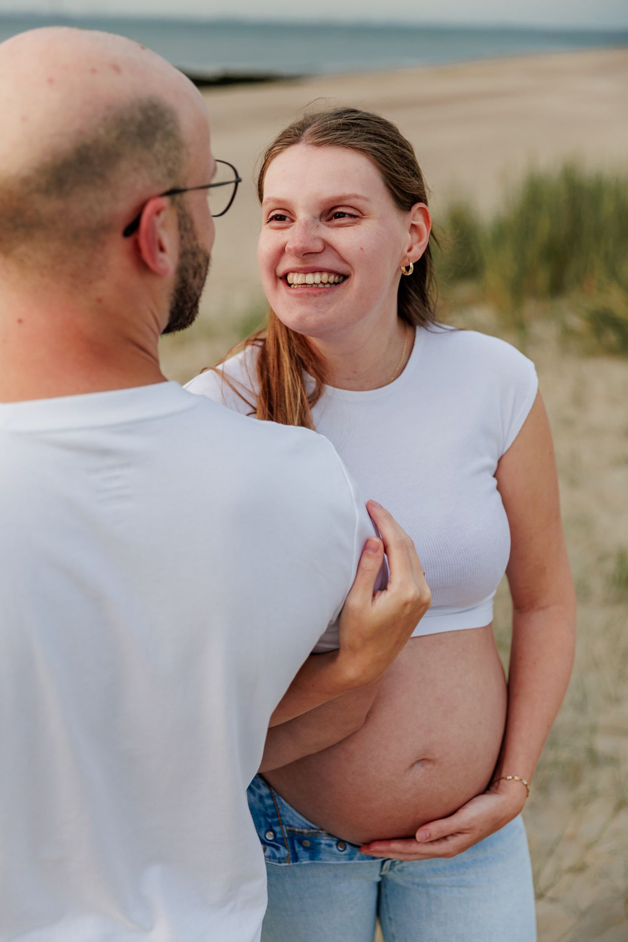 Intimate couple's maternity photoshoot showing tender moments in white and denim attire.