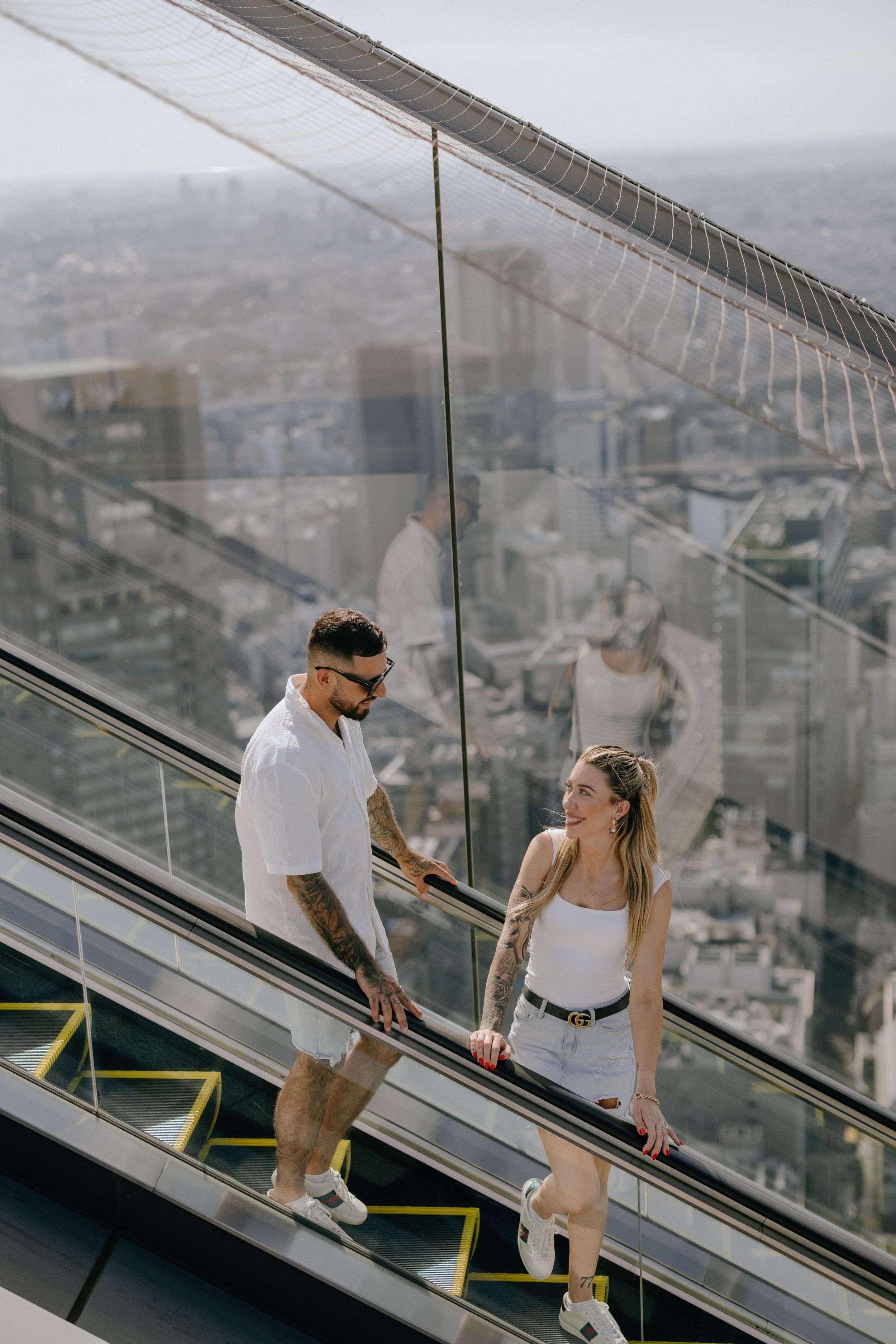 A couple sharing a moment on an outdoor escalator with city views.