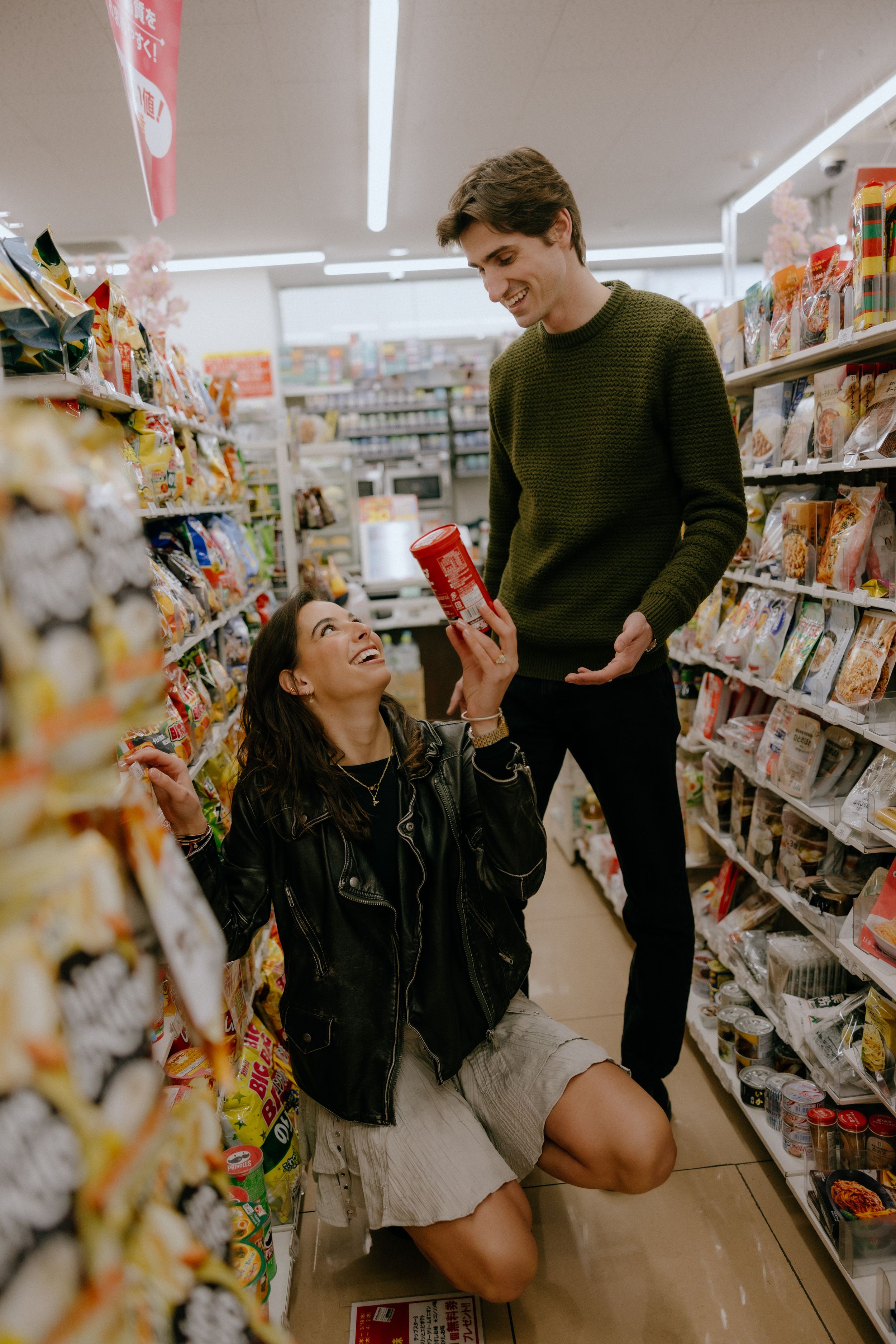 Two people interact playfully in a grocery store aisle while looking at snacks and beverages.