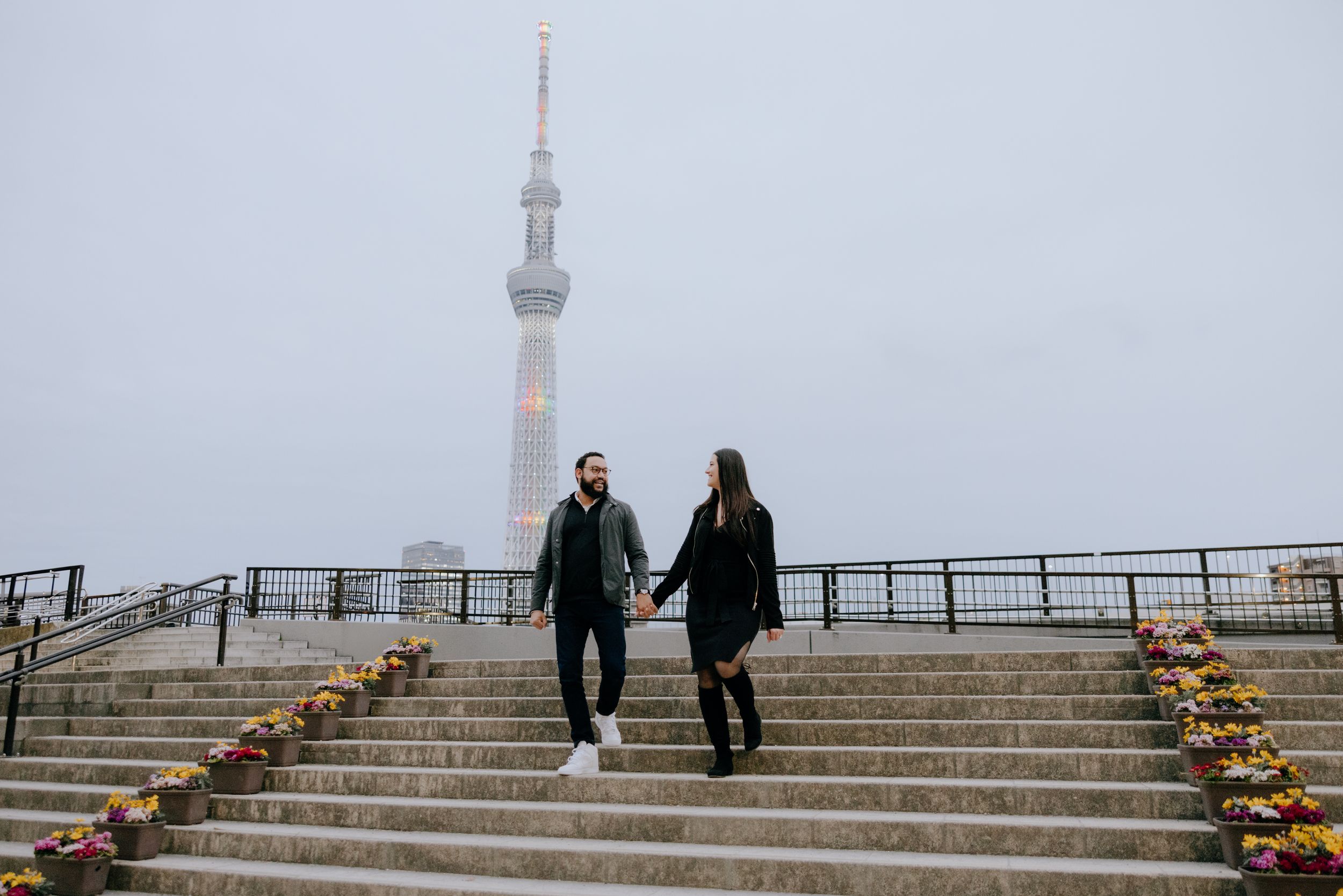 Two people walking down stone steps decorated with pumpkins with Tokyo Skytree tower visible in misty background.
