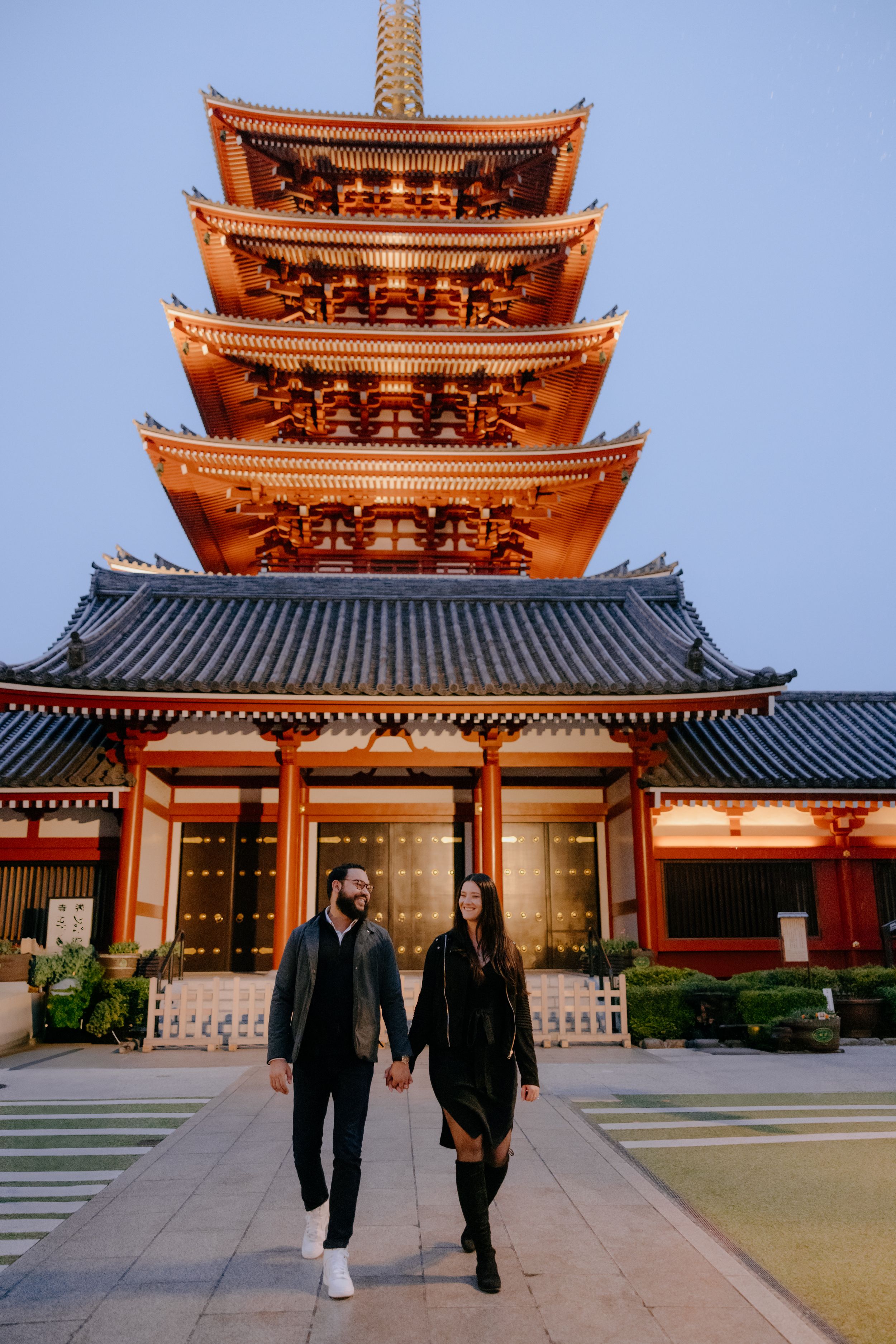 Couple walks hand in hand in front of a traditional five-story pagoda at Sensoji Temple in Tokyo, Japan during dusk.