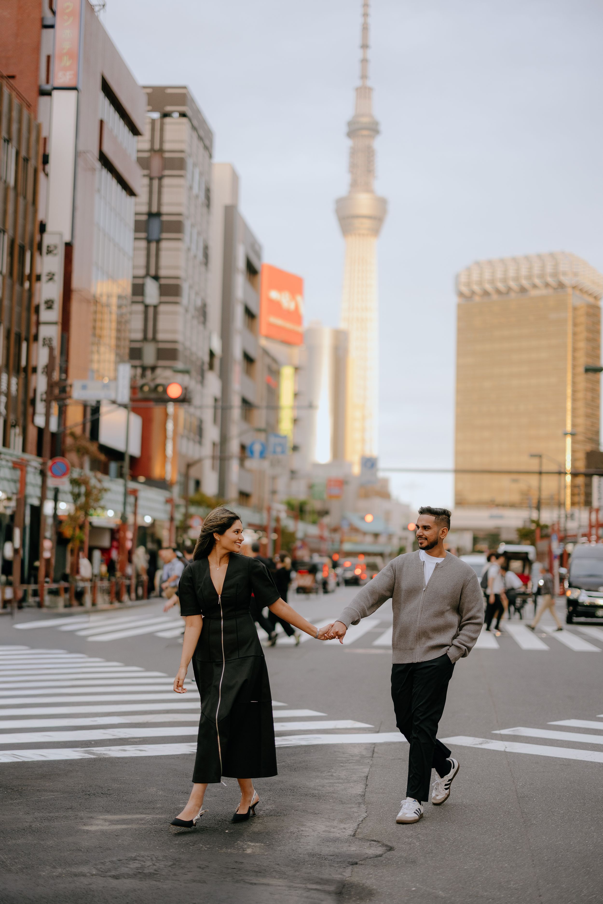 Two people playfully interact on a Tokyo street with the iconic Skytree tower visible in the background.