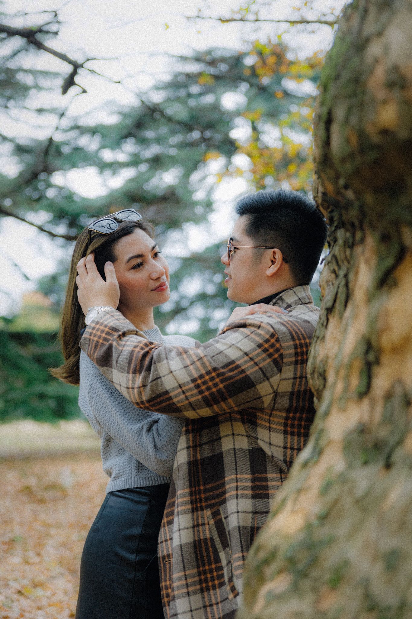 A romantic moment captured between a couple near a large tree in autumn.