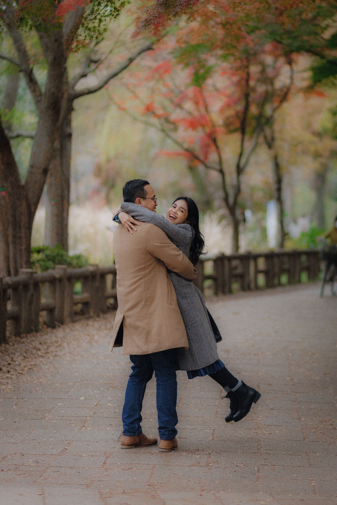A joyful embrace on a tree-lined path with autumn foliage overhead.