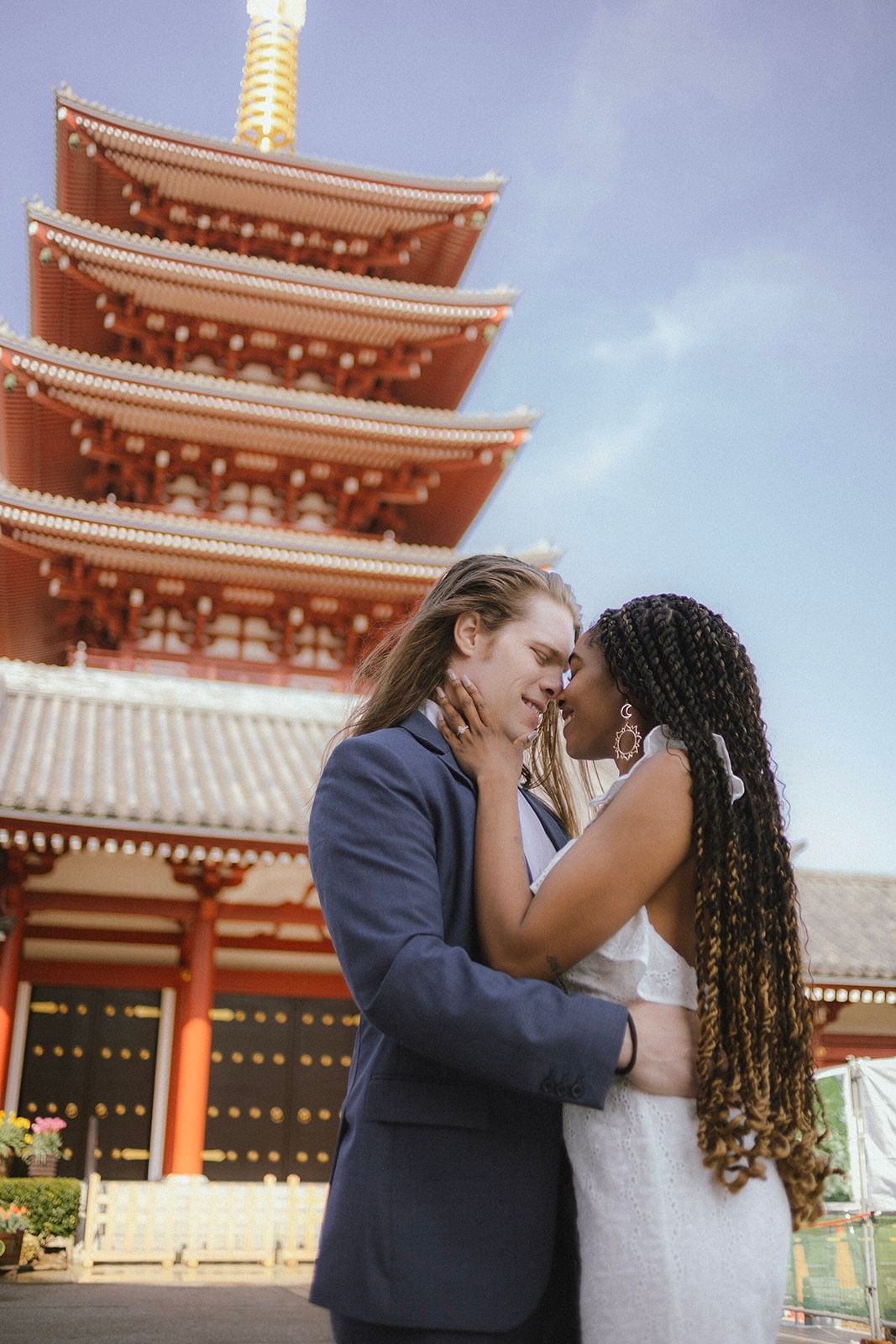 A romantic moment in front of a traditional Japanese pagoda on a cloudy day.