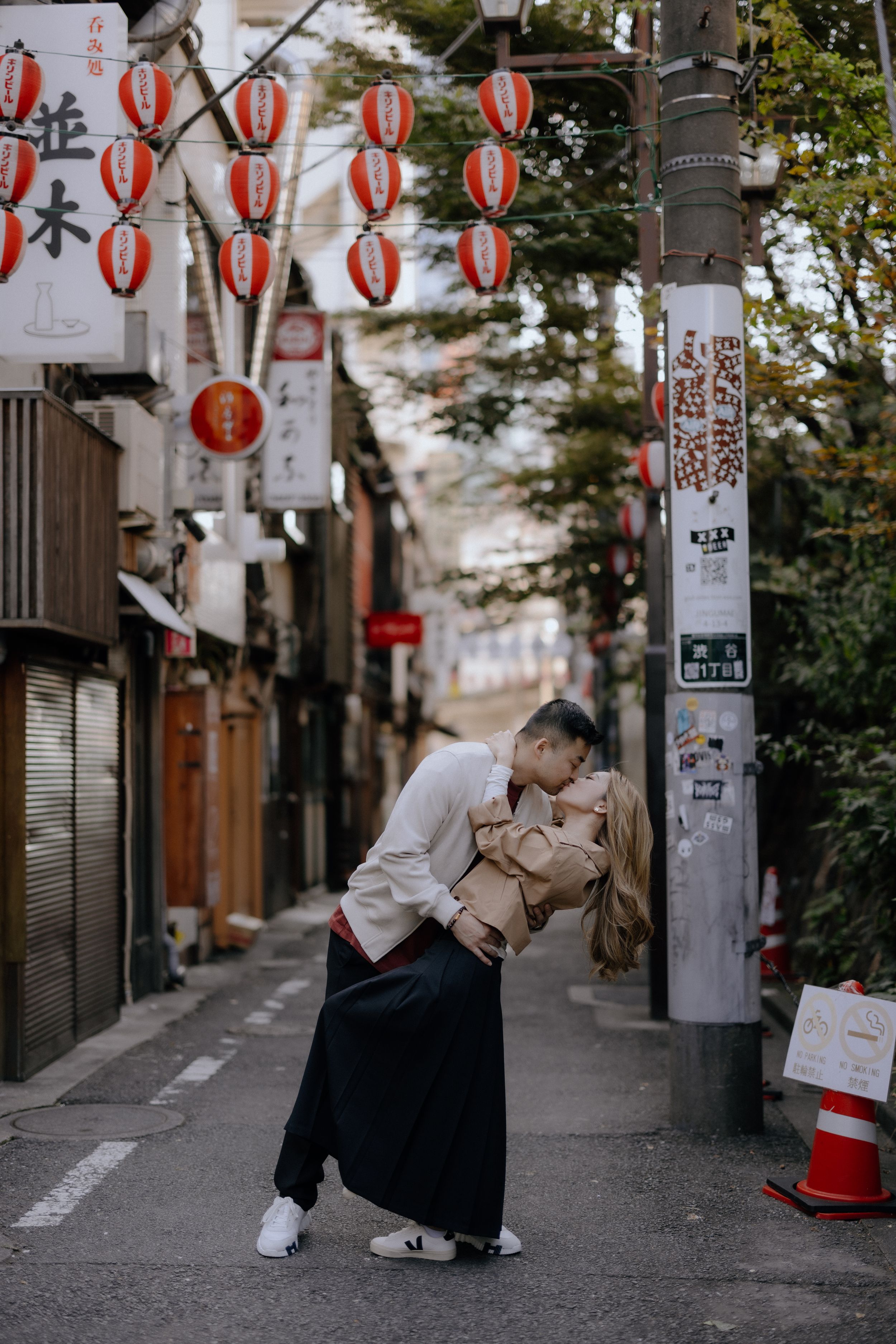 A romantic moment captured in a quiet Tokyo alley decorated with traditional red lanterns.