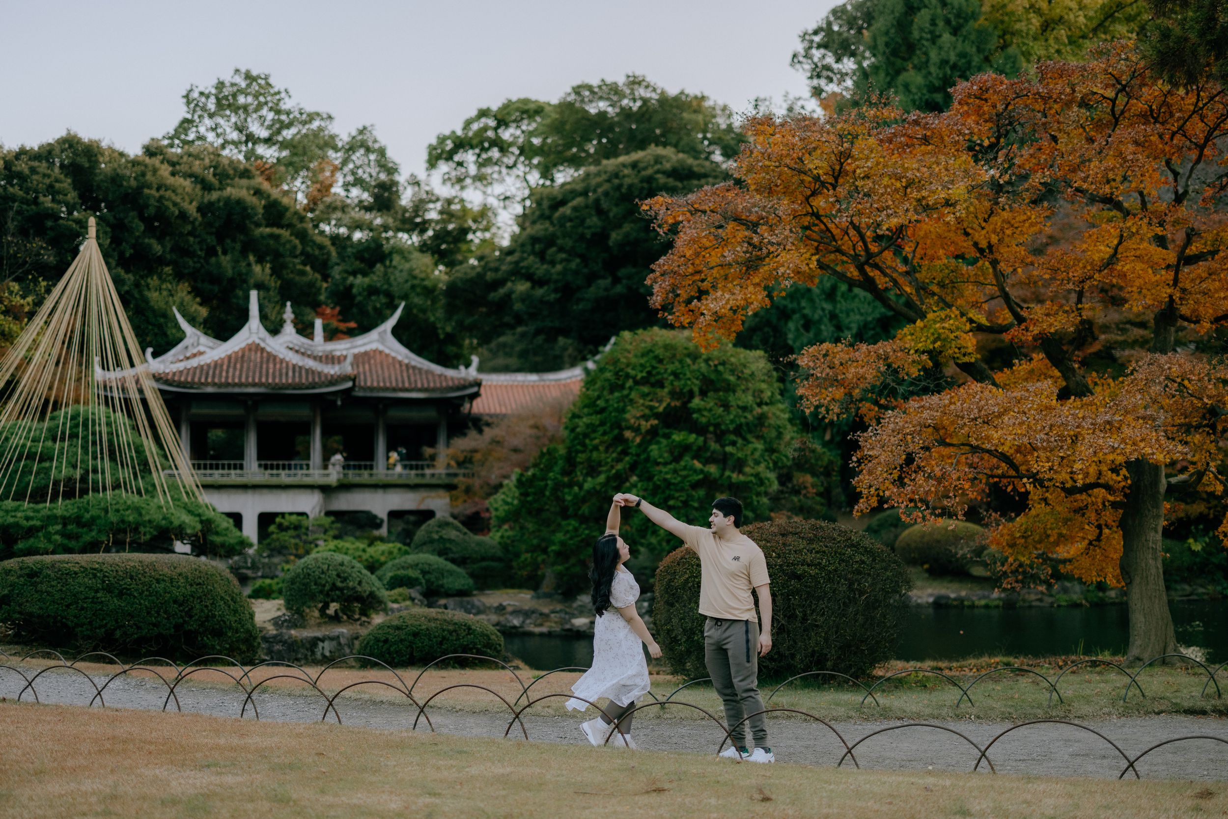 Two people walk near a traditional Japanese pagoda amid autumn trees and garden features in a serene landscape a couple walks along a path