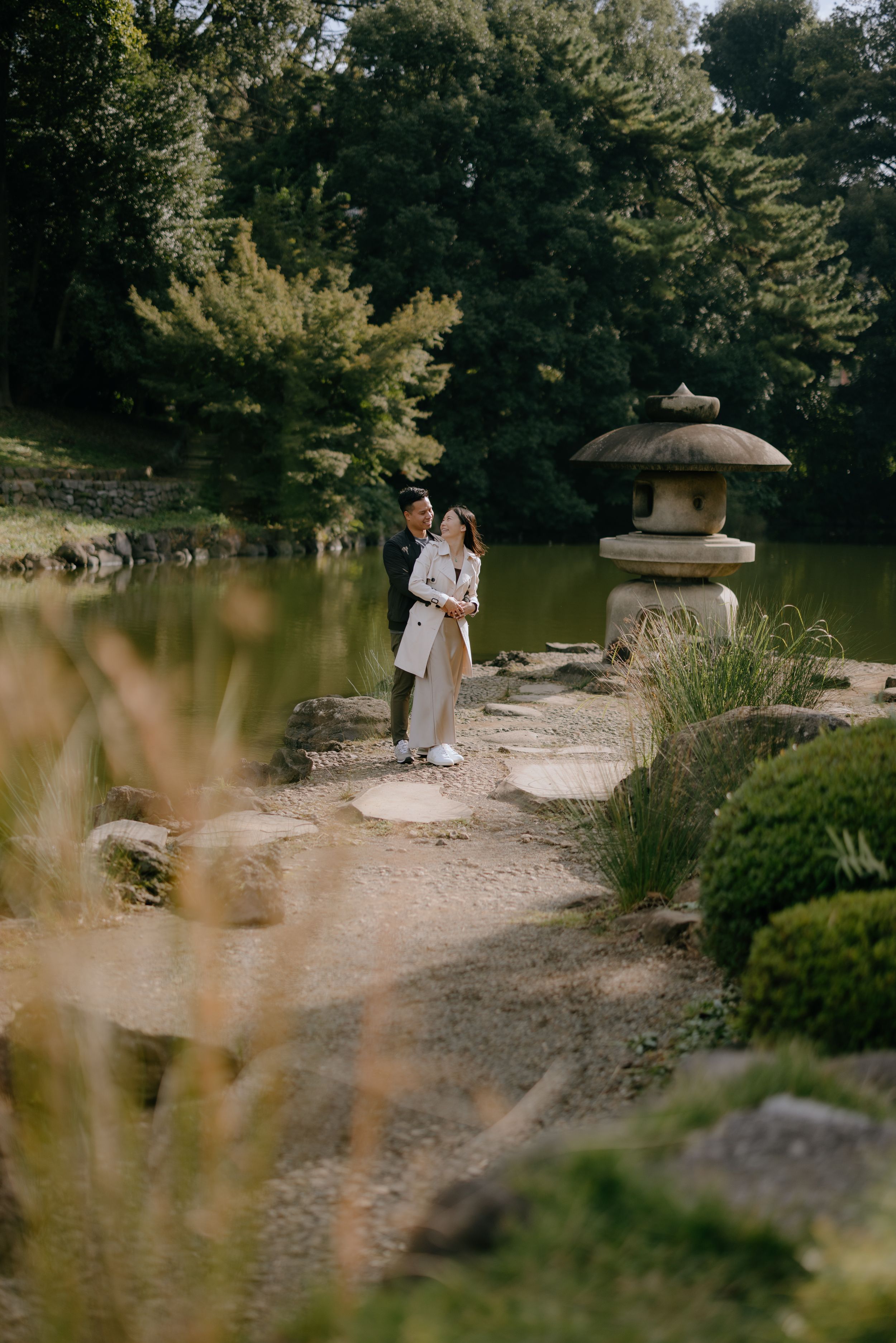 A couple stands by a traditional stone lantern in a peaceful Japanese garden setting.