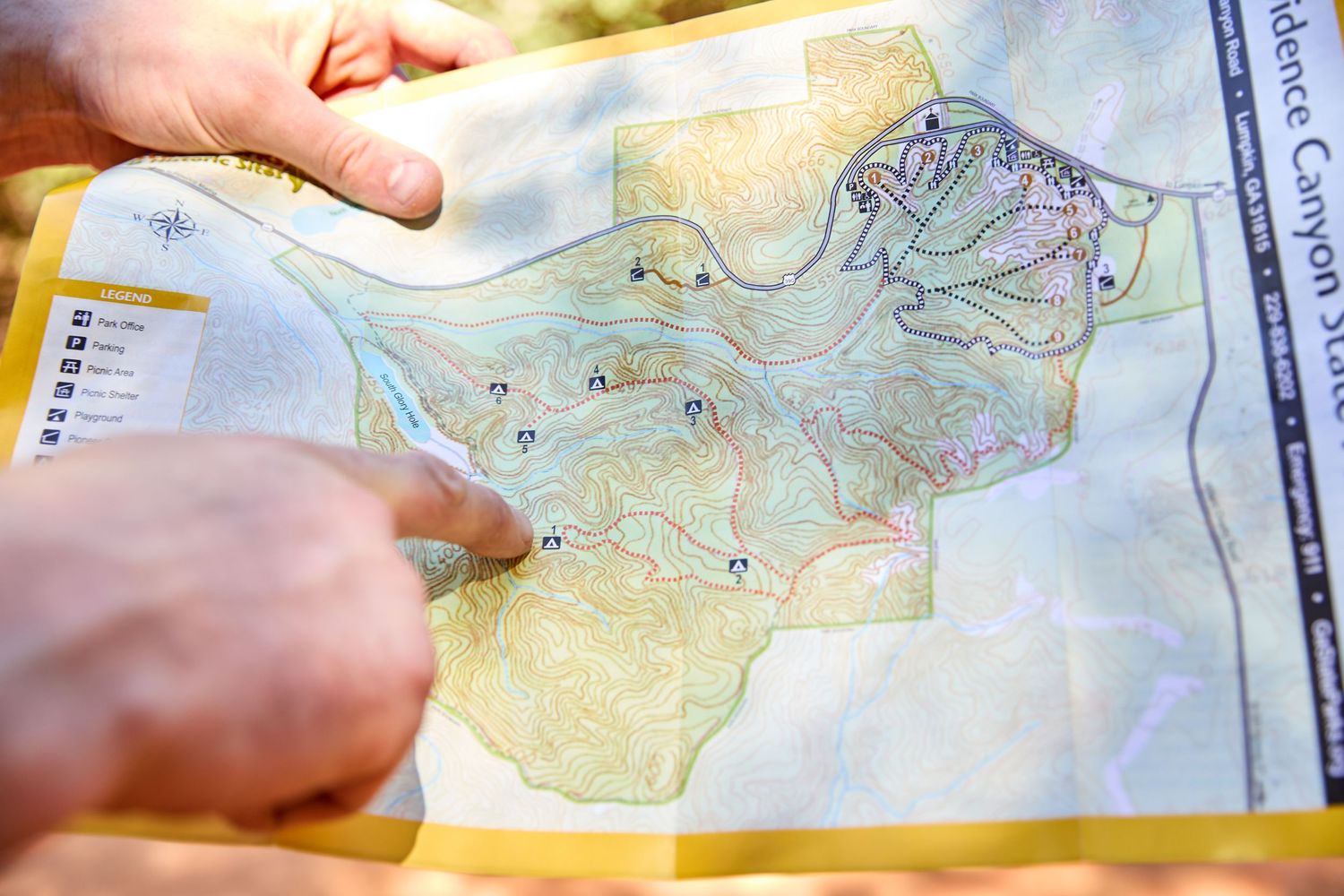 Hands holding up a translucent trail map showing topographical features and paths.
