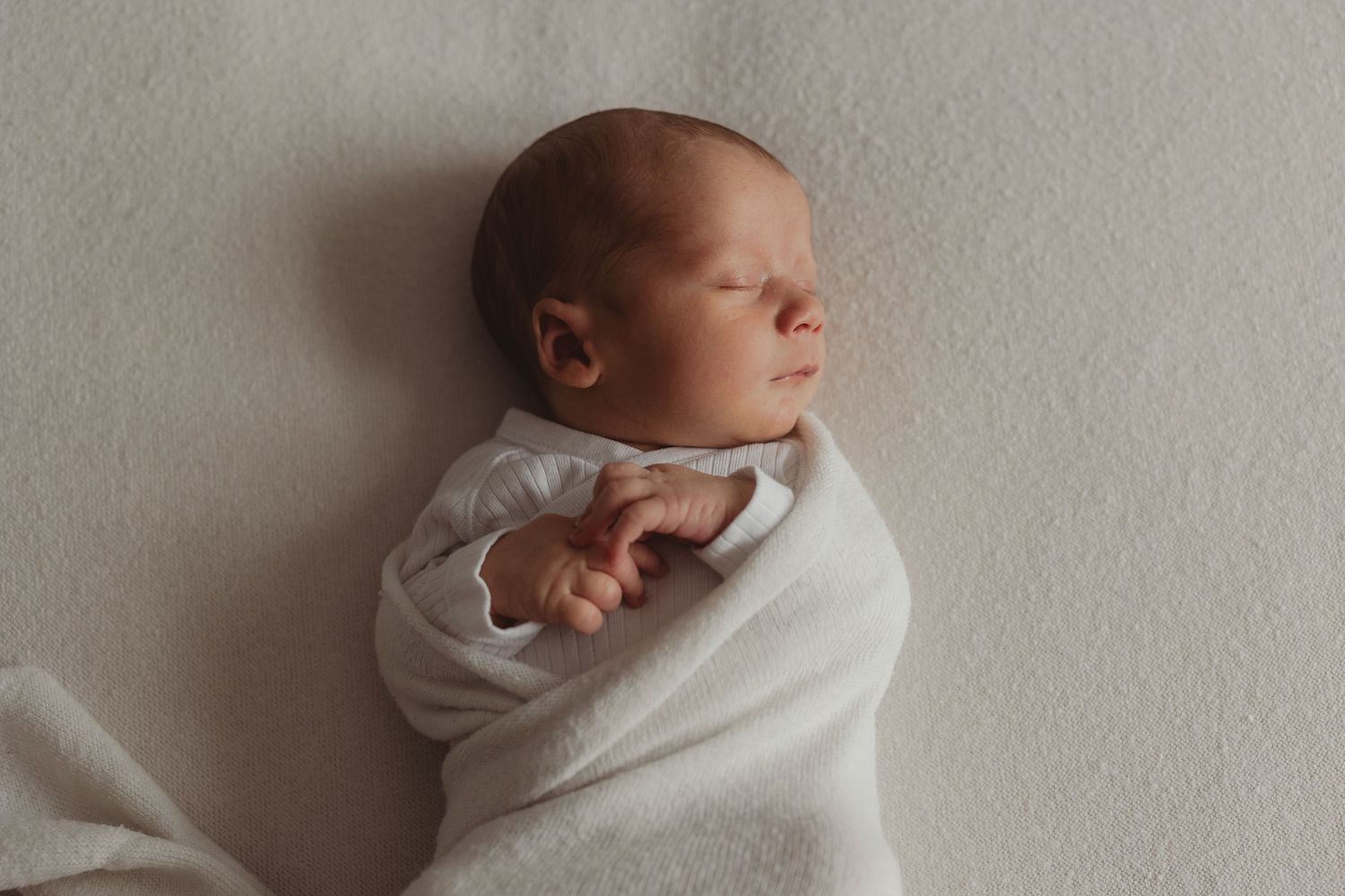 Swaddled newborn baby sleeping on a professional cream beanbag backdrop, captured during a mobile newborn photography session in Bristol.