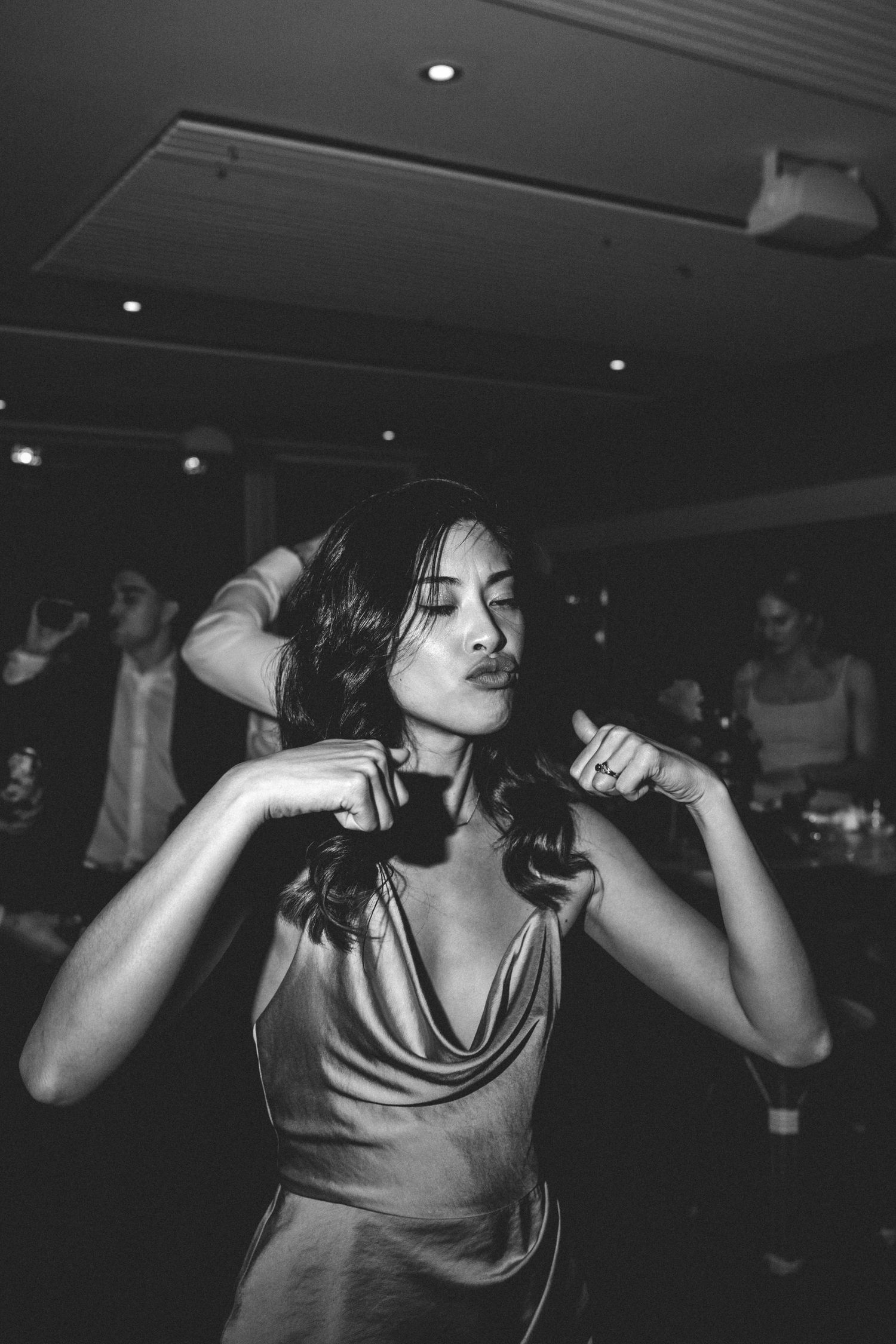 A woman in a satin dress dances gracefully under dim lighting at a party.