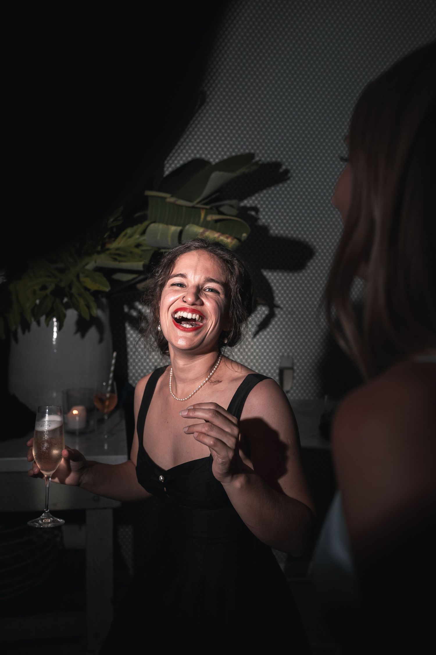 A joyful woman laughing while holding a wine glass at a moody lit party.