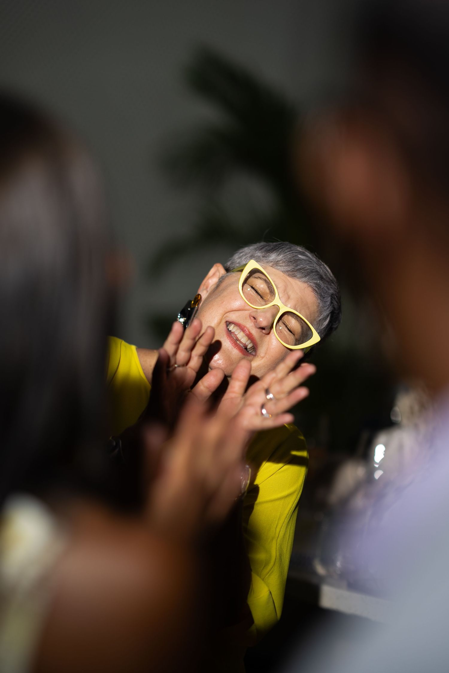Person in yellow with glasses expressing joy in a moody party setting.