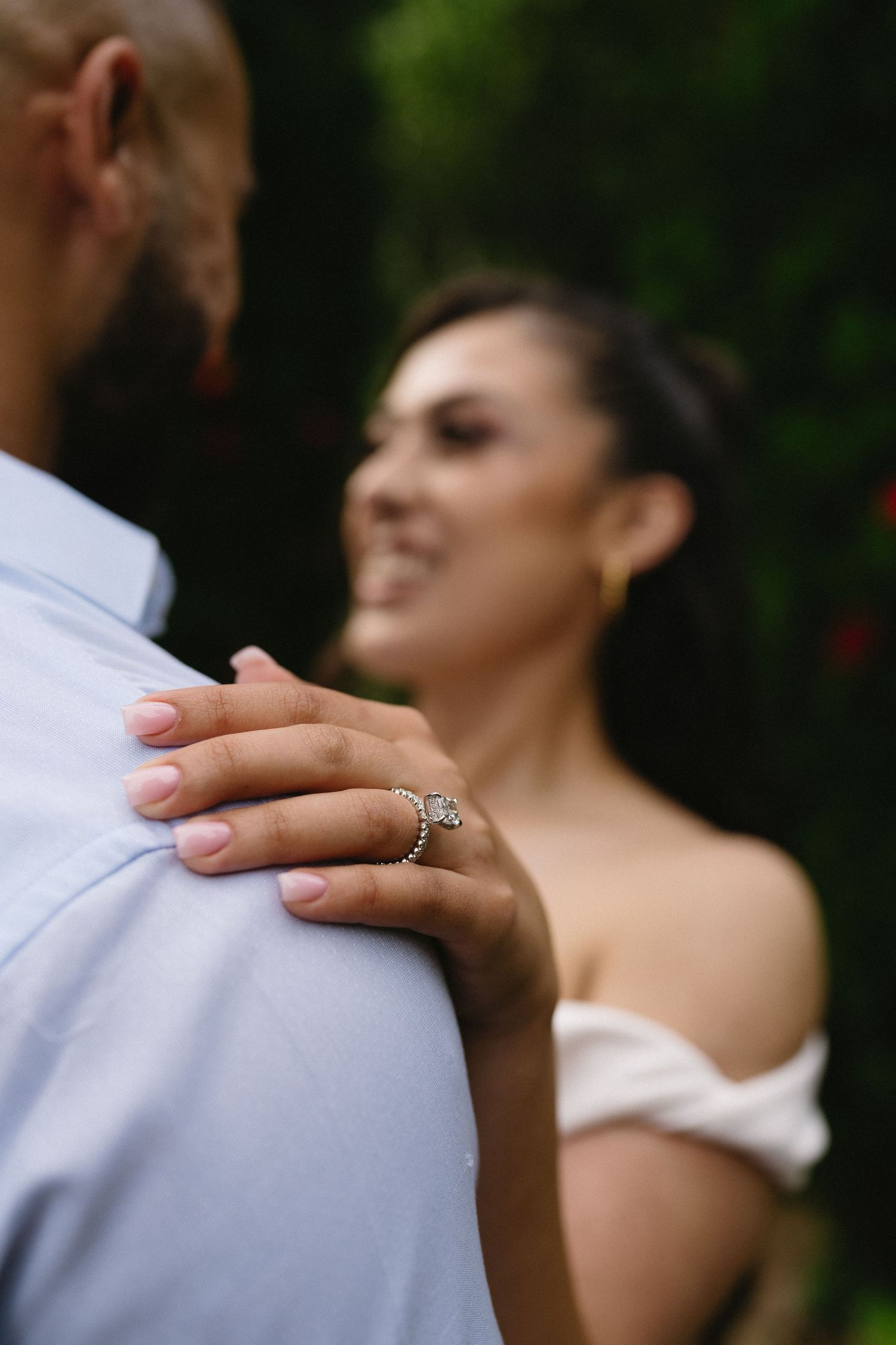 Close-up of an engagement ring as a couple embraces in an outdoor garden.