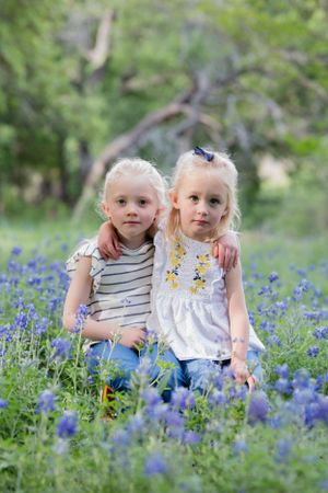 Two young children sit together in a beautiful field of blooming bluebonnets on a spring day. Cedar Park Bluebonnet Mini Session
