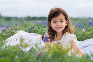 Bluebonnet Mini Session Cedar Park Brusy Creek TX A child laying in a field of bluebonnet wearing a white dress on a sunny spring day.