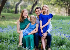 A family sits together in a field of blooming bluebonnets on a sunny spring day. Photoshoot at your house. Bluebonnet Mini, cedar Park Texas