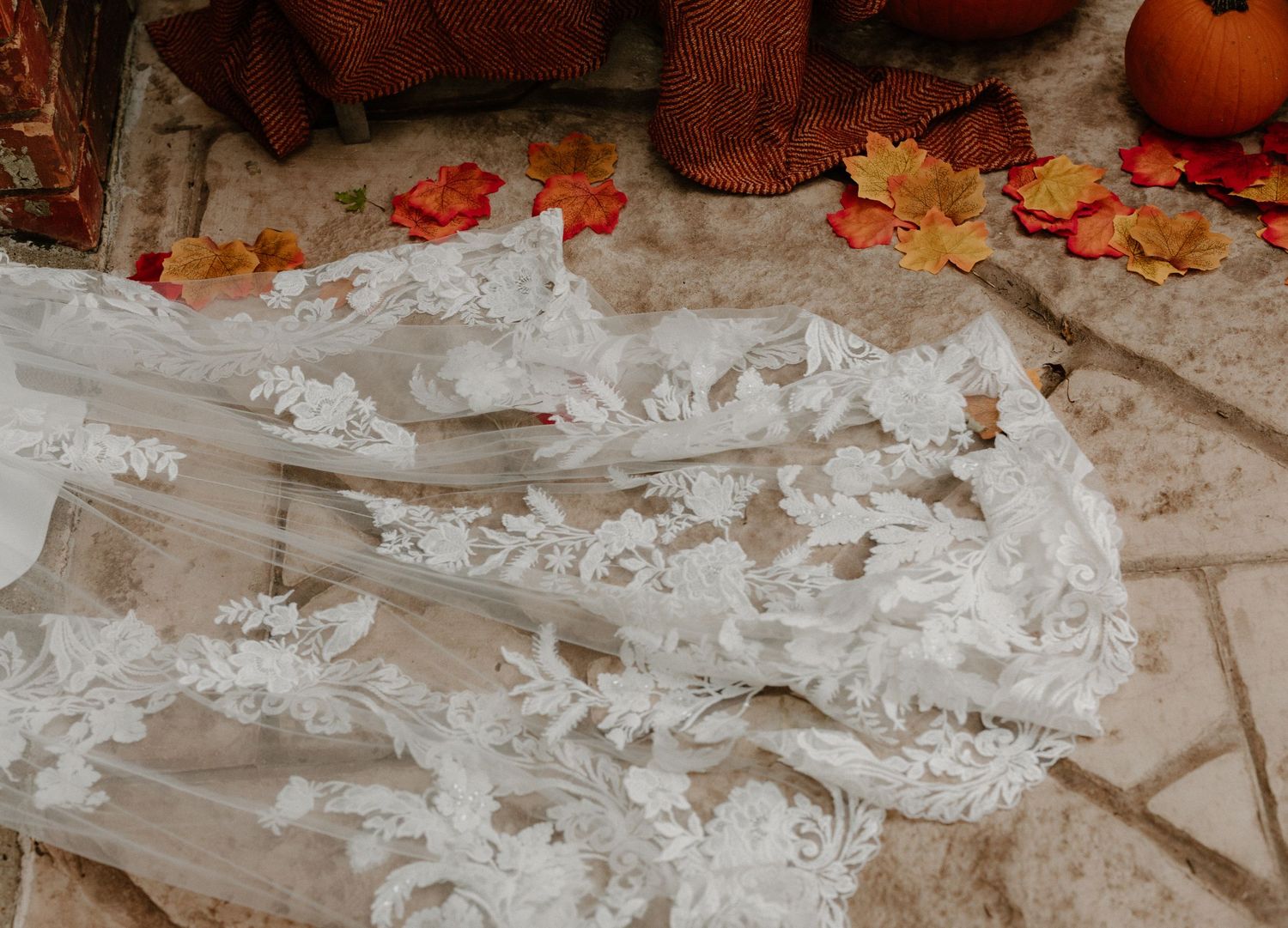 Delicate white lace fabric arranged on a stone surface with autumn leaves scattered around.