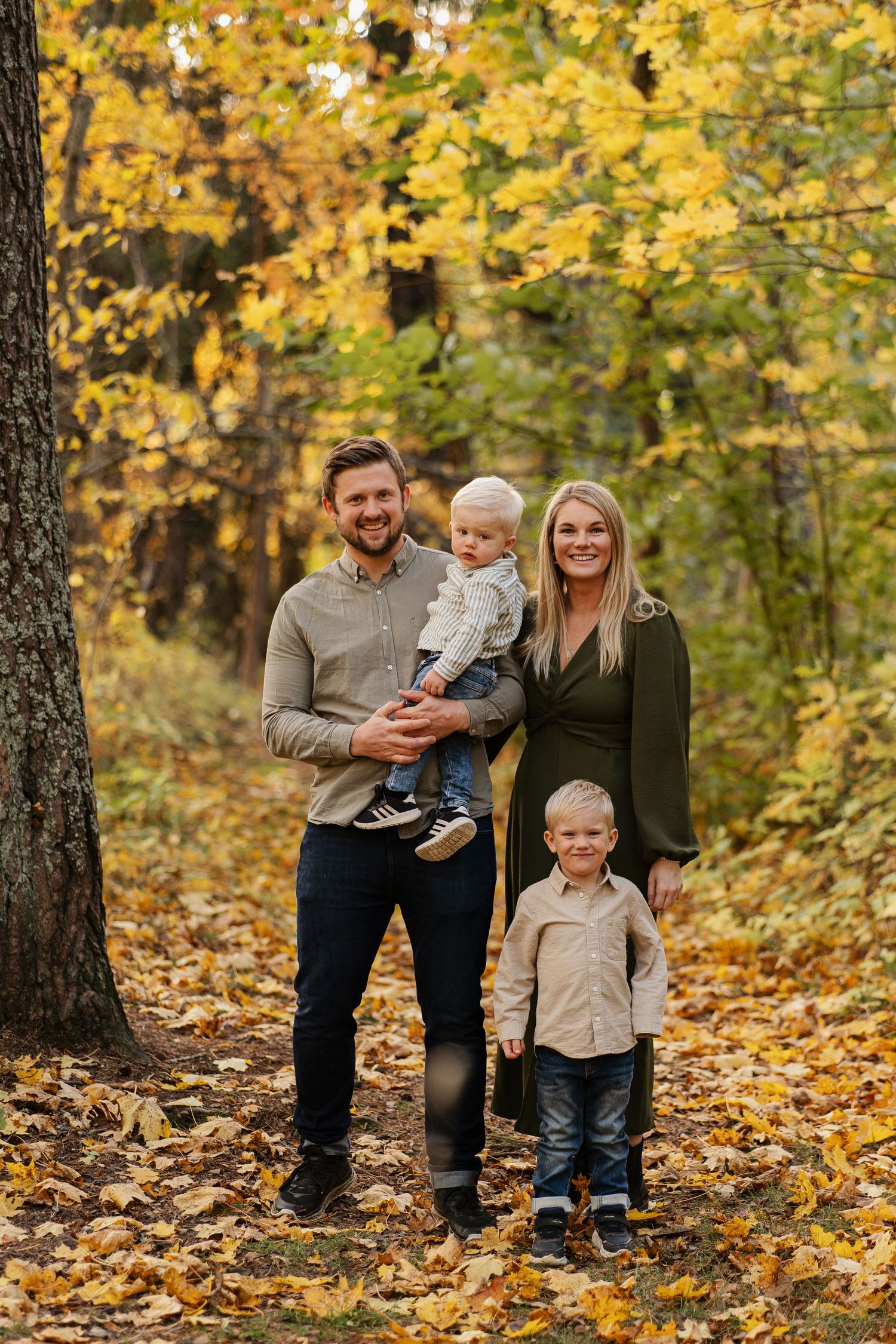 Familjeporträtt och de är omgiven av gyllene höstlöv i skogsklädda skogar. - Fotograf Emma Matkoski