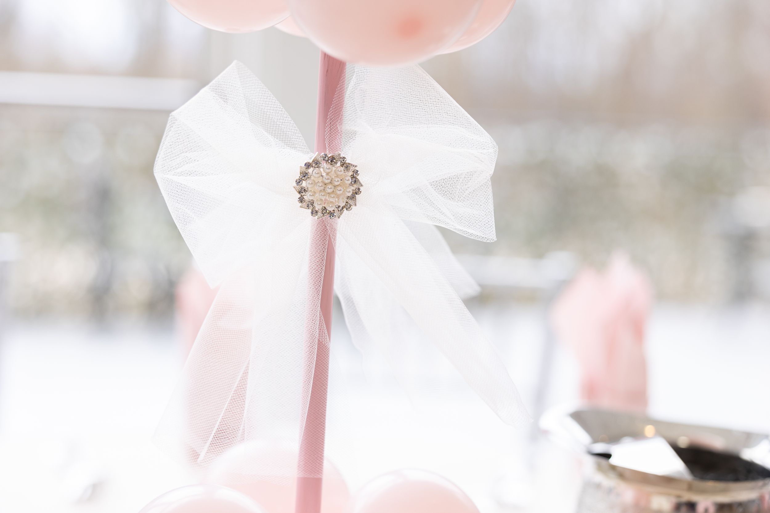 Close-up of white satin bow with rhinestone brooch on pink stick.