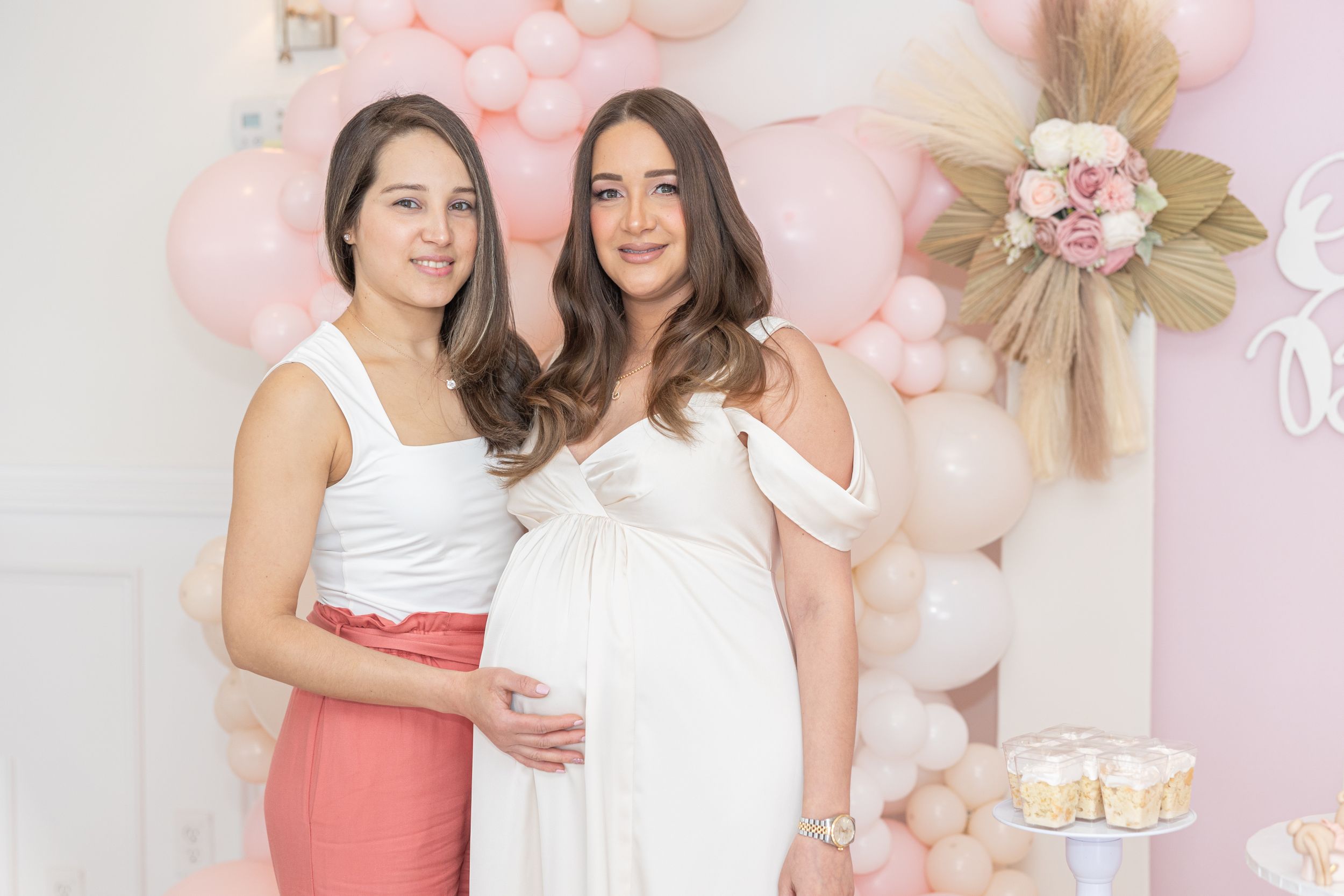 Baby shower celebration with pink and white balloon decorations and elegant cake display.