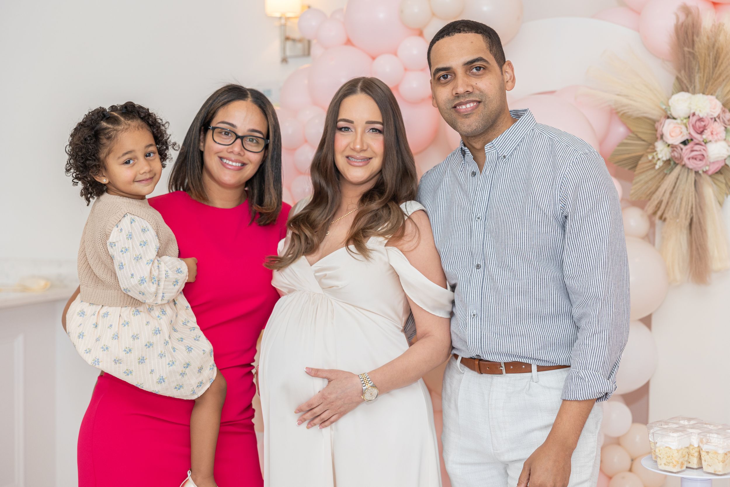 Baby shower celebration with pink balloon arch and white tiered cake display.