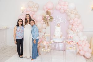 Baby shower celebration with elegant pink balloon arch and white cake display.