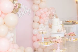 Pink and white balloon arch display with elegant baby shower dessert table featuring tiered cake.