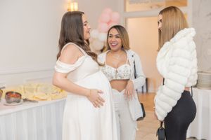 Three women gather around and celebrate at a festive baby shower party.