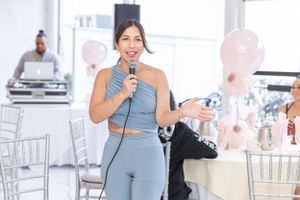 Woman in blue activewear outfit speaking into microphone at party with balloons.
